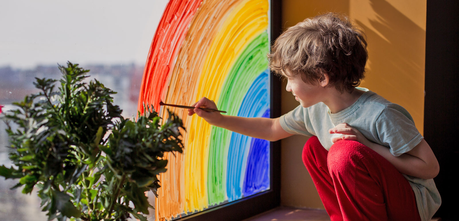 boy painting a rainbow on a window