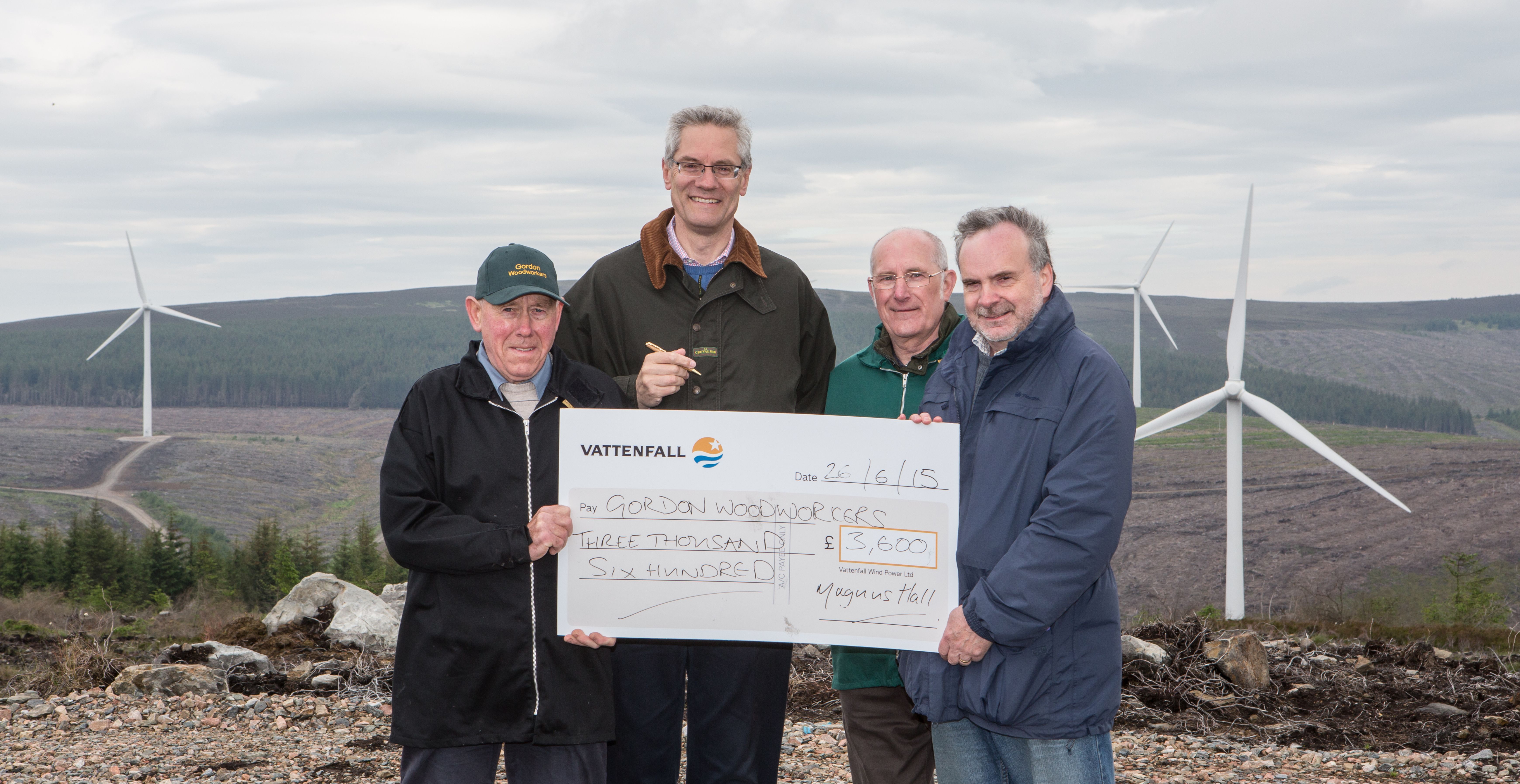 A group of people holding a cheque in front of a windfarm.
