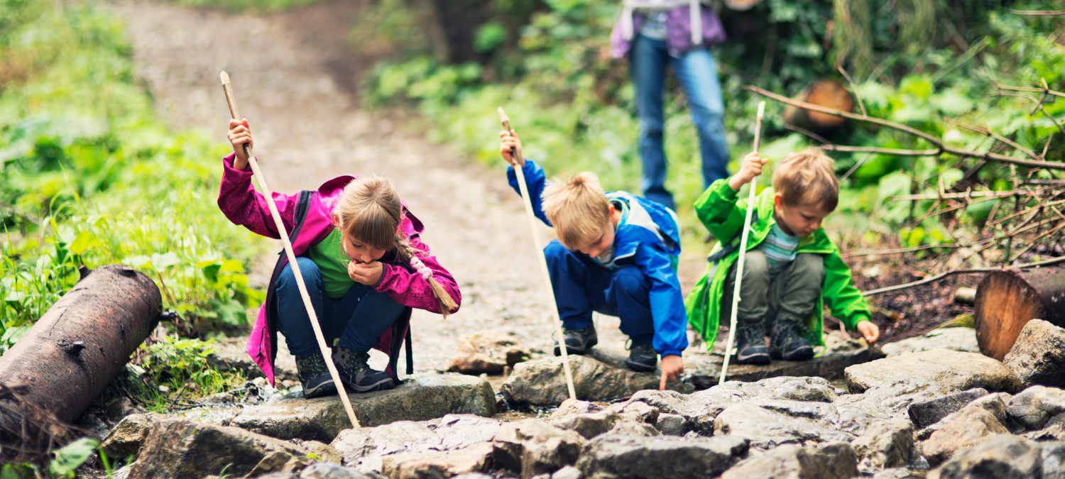 three kids wearing bright coats playing on a log in a forest